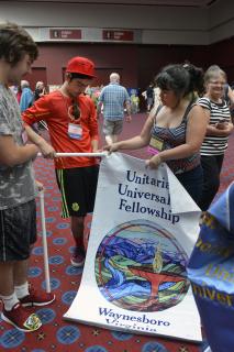 Several young people work together to thread their congregation's banner onto a GA banner pole