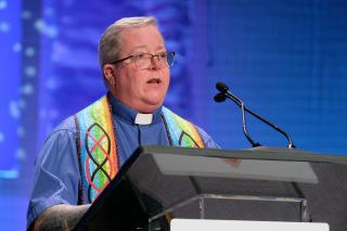 A preacher in a colorful stole speaks at the podium