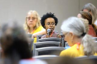 An African American woman holds a microphone and addresses a GA workshop from the audience