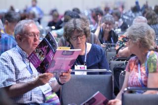 A GA attendee consults his pink printed program book for GA information.