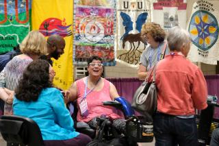 A group of GA attendees laugh during an Exhibit Hall poster session. Colorful congregational banners form a vibrant backdrop.