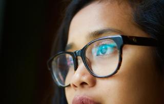 A close-up of a person wearing glasses, gazing into the distance.