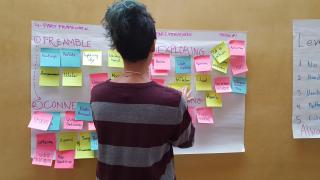 A UU youth stands and looks at interactive post-it notes describing elements of worship.