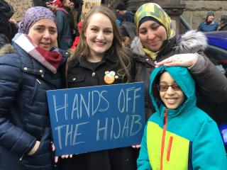 Four women gather around a sign that says "Hands off the Hijab" at a protest against the immigration ban by Donald Trump in Boston's Copley Square.