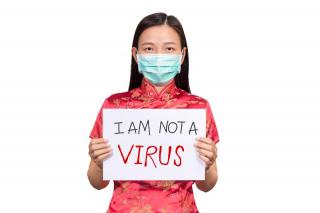 young Asian woman wearing medical mask holding sign "I am not a virus"