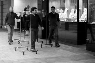 a trio of men wheel empty garment racks past a storefront