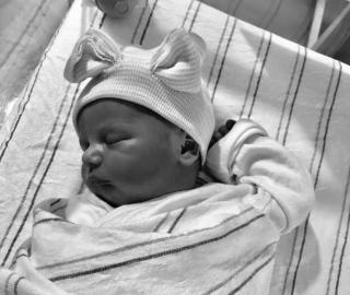 A newborn infant swaddled in blankets, sleeping, wearing a hat.