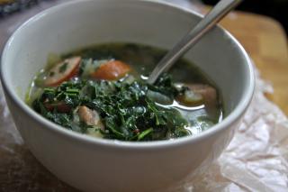 a bowl full of kale soup, spoon sticking out