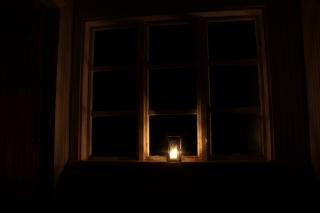 A candle in a lantern burns against a dark set of window panes.