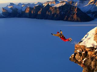 Person leaping off a ledge with snow in the mountains