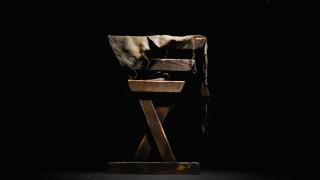In stark light, against a black background, a simple wooden manger