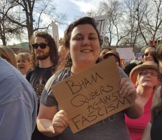 A woman holds a cardboard sign, "B'ham Queers against Fascism," at a Women's March in Alabama.