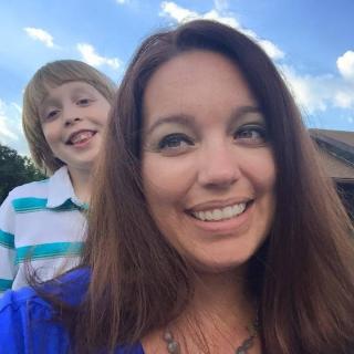 Melissa Gibson smiles, a blue sky behind her, with a smiling child looking over her shoulder at the camera.