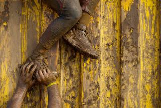 A pair of muddy arms reaches up to push a muddy foot, as if helping someone climb a wall.