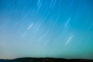 A time-lapse photo of a sky at twilight, with the curved lines of stars' movement.