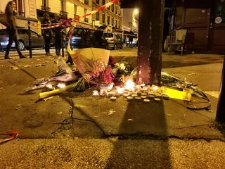 At the base of a street sign, a collection of small candles and flowers to honor victims of a terrorist bombing
