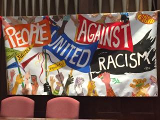 A colorful, whimsical banner hangs on a church chancel: "people united against racism"