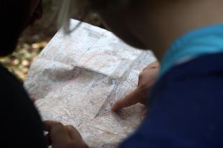 Two people, out of frame, examine a wilderness map, while one points to a spot on the map
