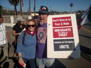Two people pose for photo, one holds a sign supporting immigrants