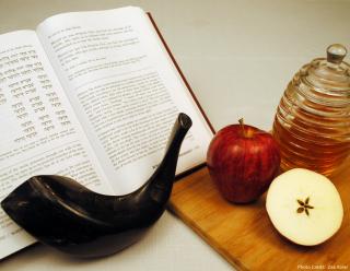 a jar of honey, two apples, a shofar, and an open Torah set the scene for Rosh Hashanah