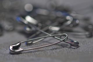 a silver safety pin rests in front of a blurred pile of its mates