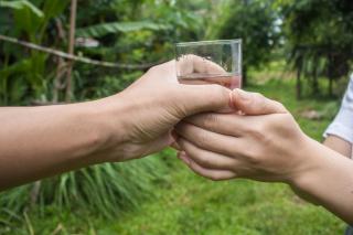 A person, with two hands, receives a glass of water from another person. 