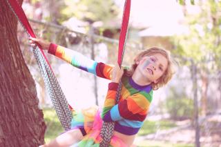 A gender nonconforming 10 year old child playing outside, with a rainbow painted on their cheek.