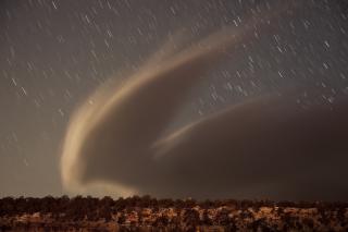 A wind-driven cloud over the south rim of the Grand Canyon, with stars in the background