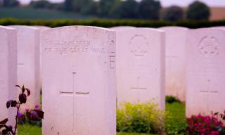 A row of white military gravestones; the closest one is engraved with a cross and the inscription "a soldier of the Great War"