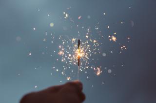 Against a dim sky, a hand holds a lit sparkler