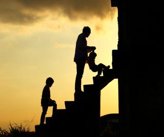 Silhouette of man walking child up steps with sky in the background.