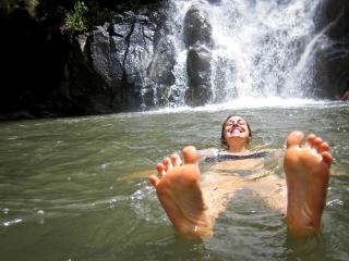 With a foaming waterfall behind her, a woman floats in water, smiling, with her bare feet floating in the foreground