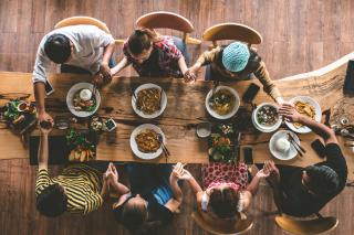From above, seven people hold hands around a table before eating.
