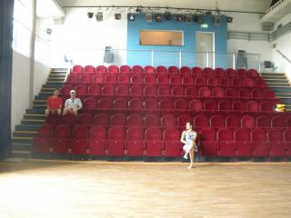 Six steeply-banked rows of red velvet theatre chairs, flanked by similarly steep staircases. 