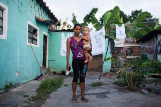 Honduran woman holding her one-year-old son next to a teal house with clothesline outside.