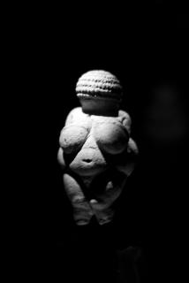 A black and white photo of the Venus of Willendorf statue, lit from above.