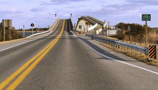 A two lane highway rises on to a steep bridge.