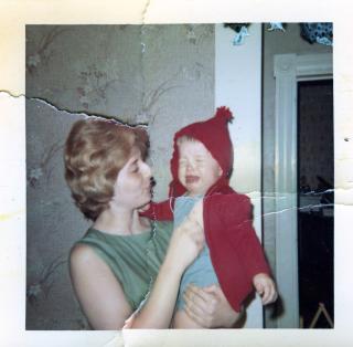 In an old photo that's been torn and taped back together, a mom holds and comforts a wailing child