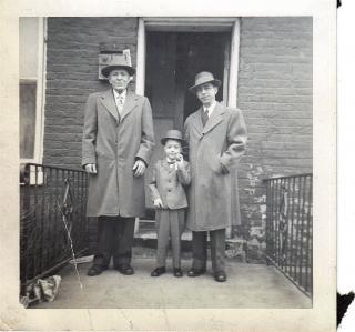 A square, faded, black-and-white photograph showing two men in overcoats, and a small boy in a suit, giving the impression of three generations.