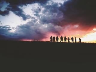 From a distance, a group of people is silhouetted by a vibrant sunset.