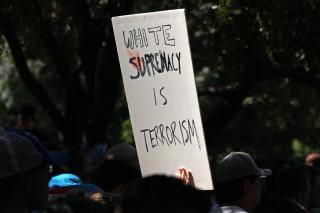 Over the heads of people at a protest, a sign on white posterboard in black marker: "White supremacy is terrorism."