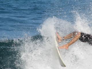 As an ocean wave splashes, a surfboard and a pair of legs are shown mid-wipeout.