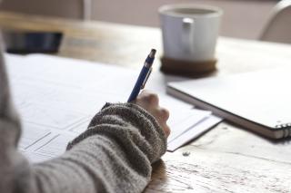 Person in sweater with hot beverage writing with a pen