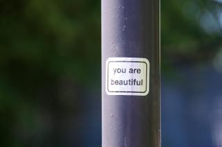 A metallic sticker that says "you are beautiful" stuck to a metal lampost