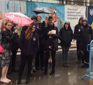 A group of youth stand outside the UN in the rain waiting to get in.