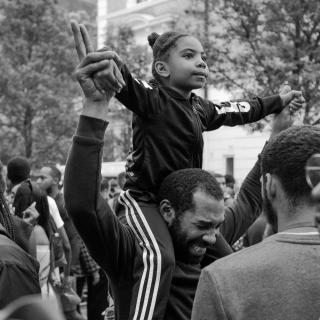 A small black child rides on their father's shoulders, as the two hold hands