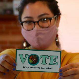 Person wearing mask holding card that says Vote