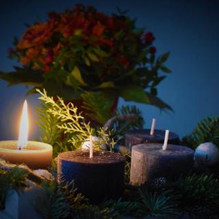 nestled into an evergreen wreath is a lit white candle and three unlit purple candles