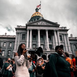Demonstrators stand in front of Capitol, one person holds a megaphone