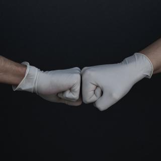 One latex-gloved hand fist bumps another latex-gloved hand